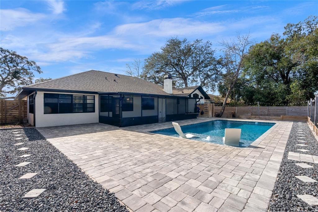 Spacious backyard featuring a newly built saltwater pool with a clean, modern design. The pool area is surrounded by a beautifully paved patio. Fenced yard offers privacy. The home's exterior includes a screened patio area and large windows overlooking the backyard, making it perfect for entertaining or relaxing.