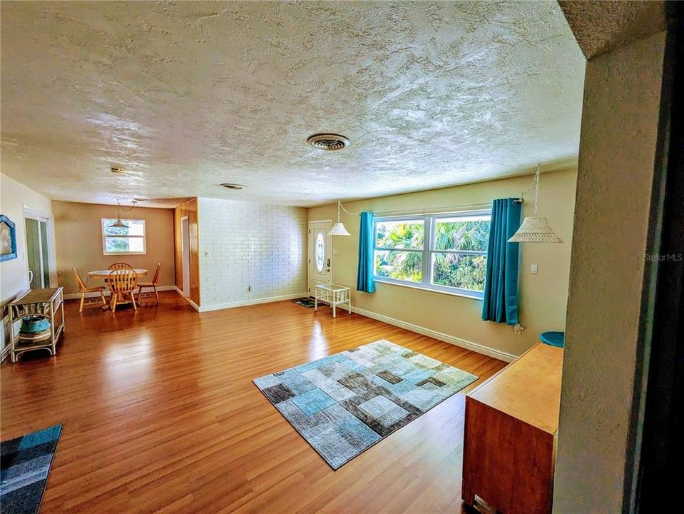 Large, bright living room with the dining room in the background. Front door is next to the large, impact glass window.