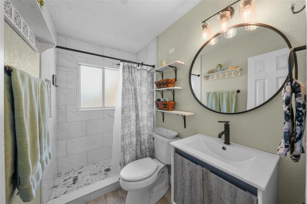 Completely updated bathroom with floor to ceiling tile shower, modern vanity with storage, and on-trend mirror and lighting