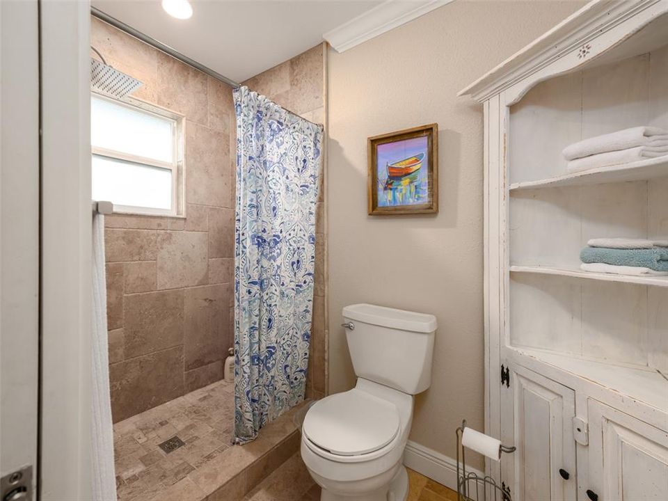 Primary shower with window and travertine tile on walls and floors.