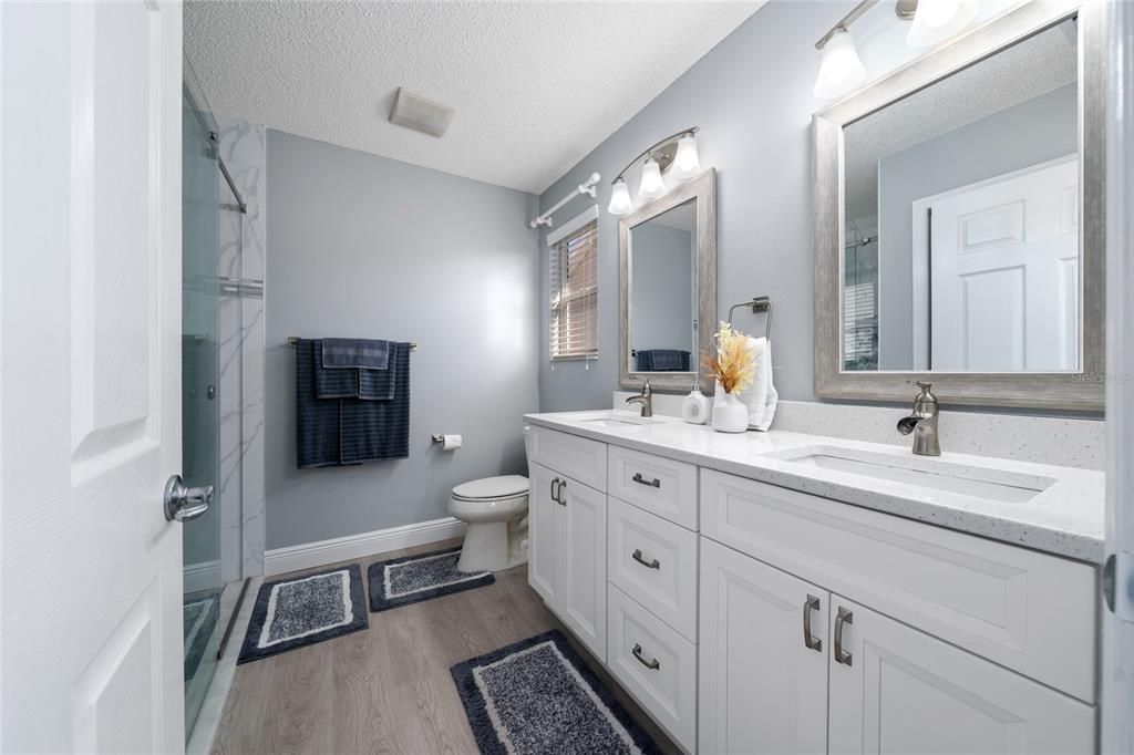 Beautiful ensuite bathroom with double sinks and mirrors, window, and glass tiled walk-in shower.