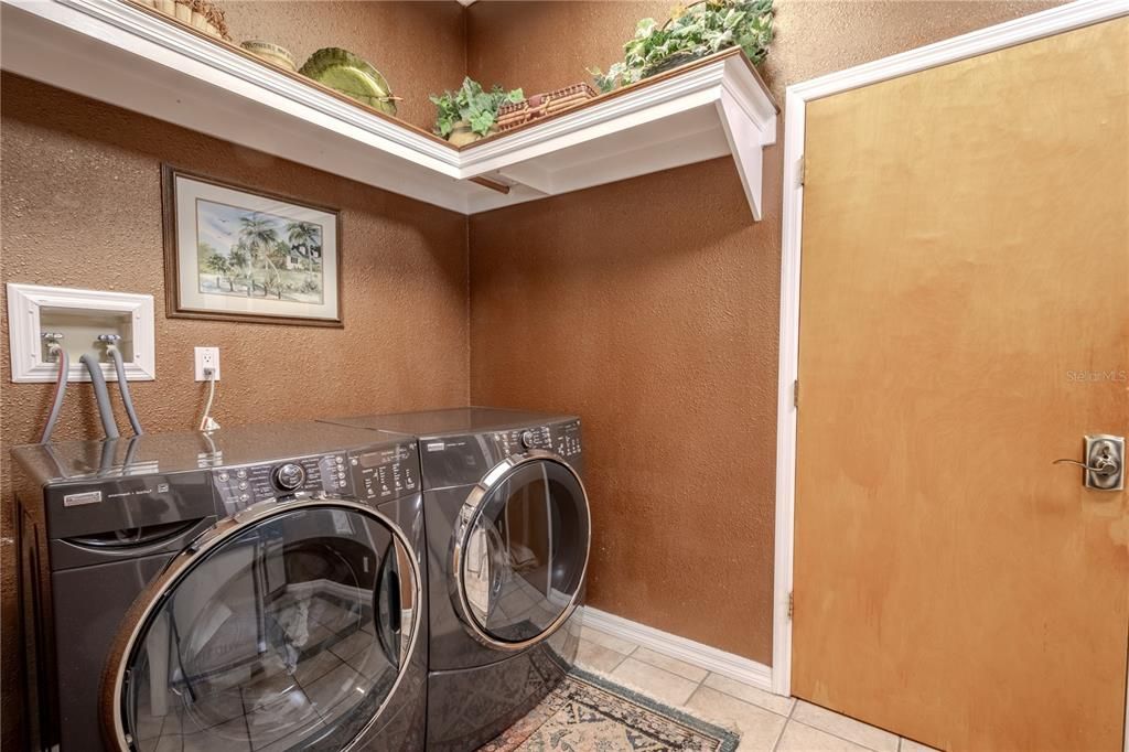 The laundry room has a front load washer and dryer and overhead shelving.