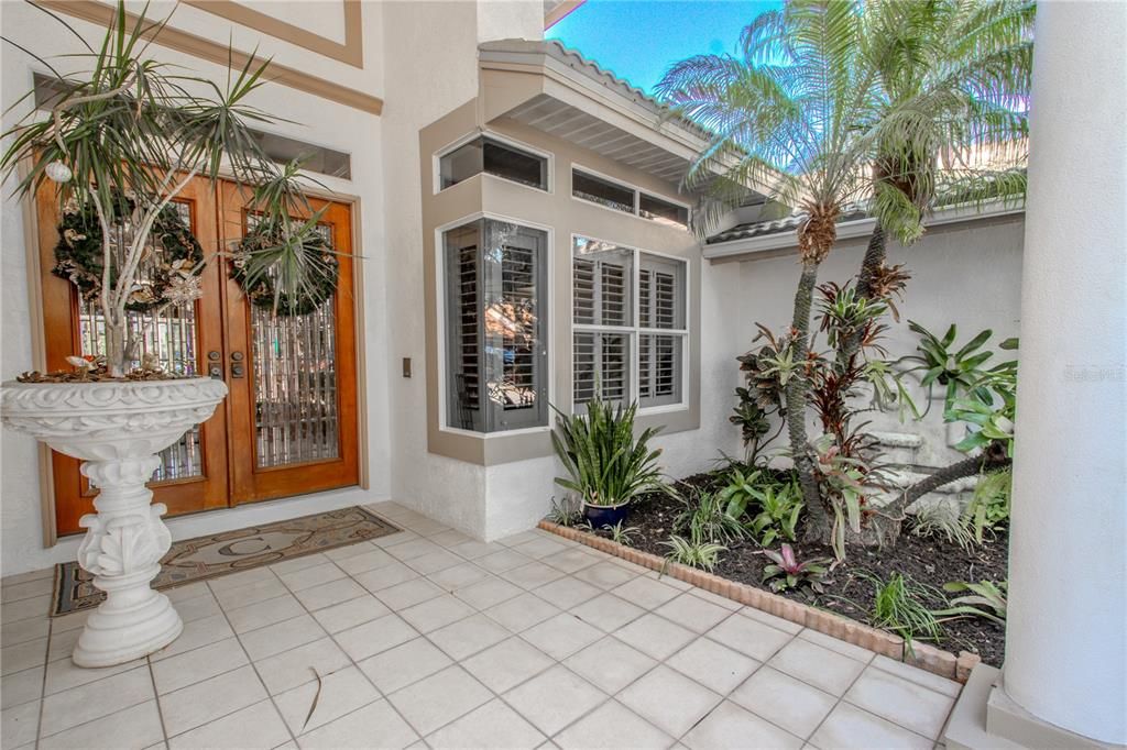 The covered front entry has a tiled floor and tropical landscaping.