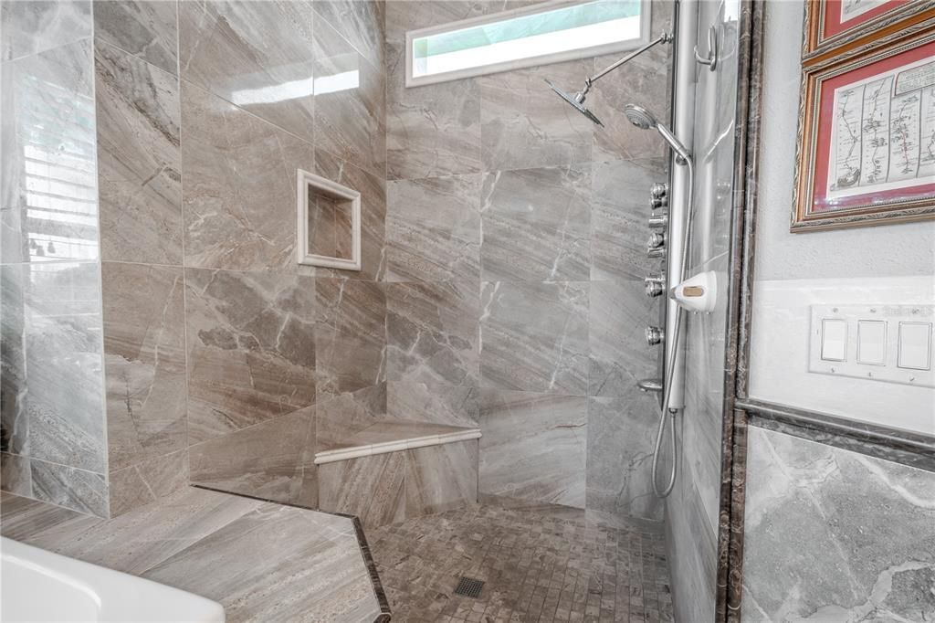 The primary ensuite showers features a built-in shower bench, multiple shower heads and a transom window.