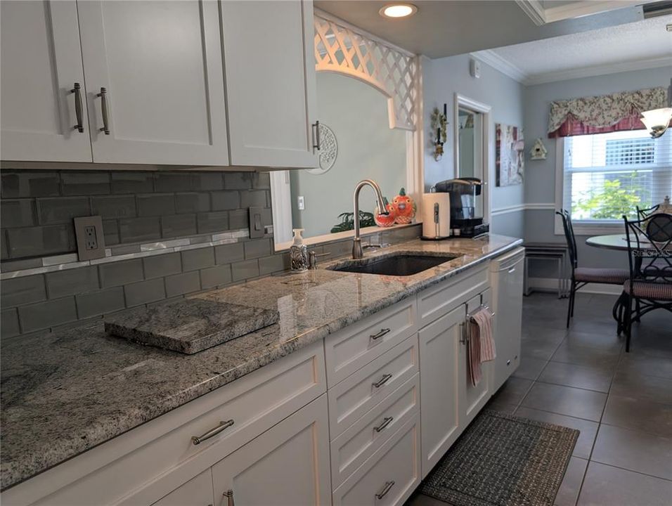 Sleek gray/silver/white kitchen features tile flooring, white shaker style cabinetry, brushed nickel pulls, glass tile backsplash and white appliances.