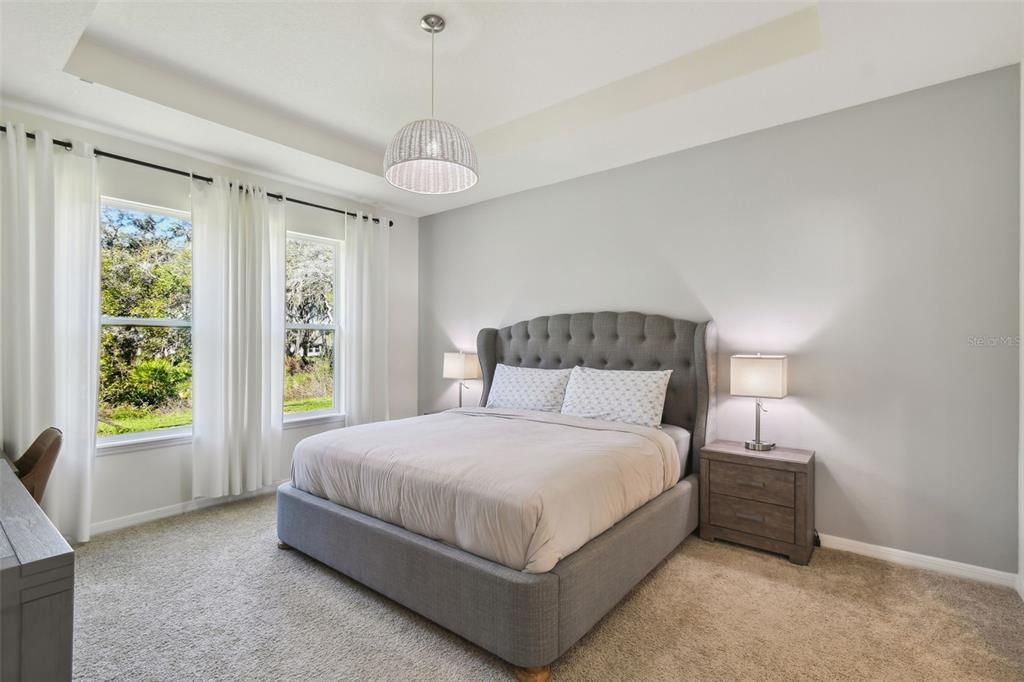 The primary bedroom features a tray ceiling and offers a lovely view of the beautiful backyard.