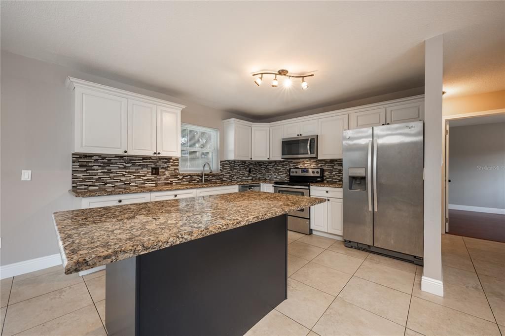 The remodeled/upgraded kitchen offers the family chef a comfortable space surrounded by beautiful solid wood cabinets (refreshed/painted 2023), STAINLESS STEEL APPLIANCES, tiled backsplash, GRANITE COUNTERS and a large island with breakfast bar seating for casual dining or entertaining!