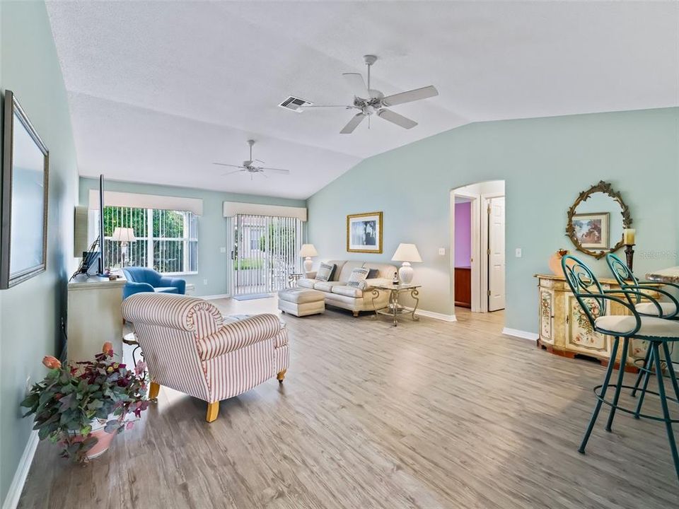 Spacious Living Room and Dining Room featuring Vaulted Ceilings, Newer Luxury Vinyl Plank Flooring and Sling Glass Doors leading out to the Lanai.