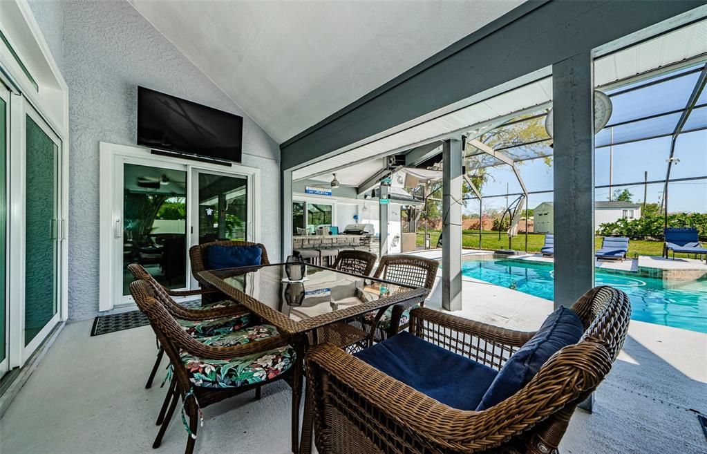 Outdoor seating near patio kitchen with grill, large TV, at poolside.