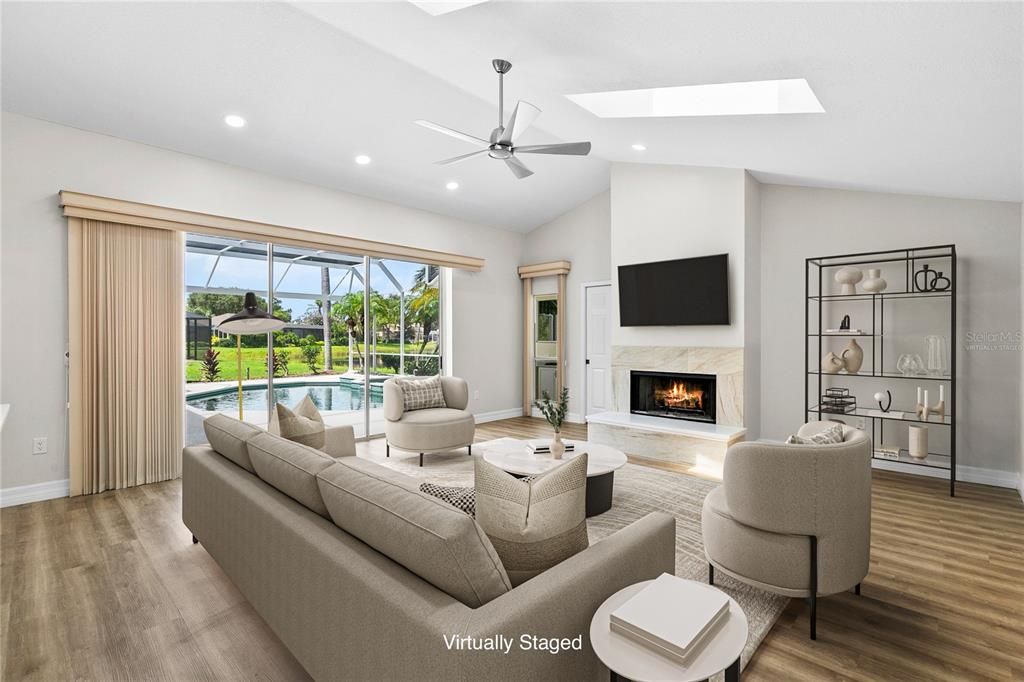 Spacious Family Room with luxury vinyl flooring, wood burning fireplace and views through the panoramic pool screen beyond. (Virtually Staged)